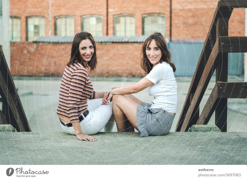 young women friends sitting on the street two people standing sister urban funny holiday travel outdoors beauty fashion life relationship portrait expression