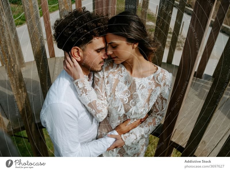 Loving young couple in wedding outfits embracing on bridge romantic newlywed embrace cuddle gentle together relationship love tender marriage sensual hug