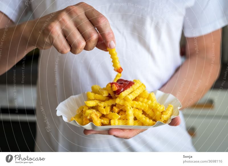 Man dips a French fry in ketchup French fries Ketchup paper plates by hand cake Close-up Fat Fast food Lunch Unhealthy Appetite Delicious Food To enjoy