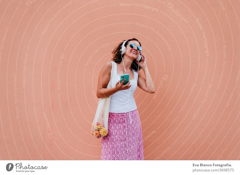 woman using mobile phone, listening to music on headset. walking by the city with cotton bag with fruit. Eco friendly, zero waste concept eco friendly shopping