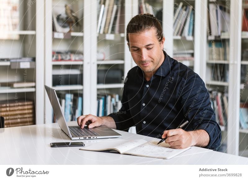 Busy male entrepreneur working on laptop in office businessman typing paperwork busy focus using take note notebook bright workspace executive gadget device