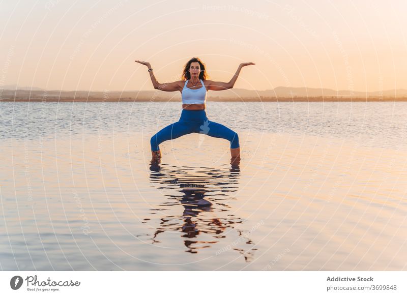 Young woman in Goddess asana reflected in lake water yoga practice pose goddess utkata konasana stand harmony spirit mind grace focus reflection balance calm