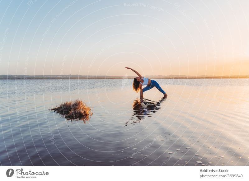 Woman in extended side angle pose reflected in lake water woman yoga practice asana utthita parsvakonasana stand harmony spirit mind grace focus reflection