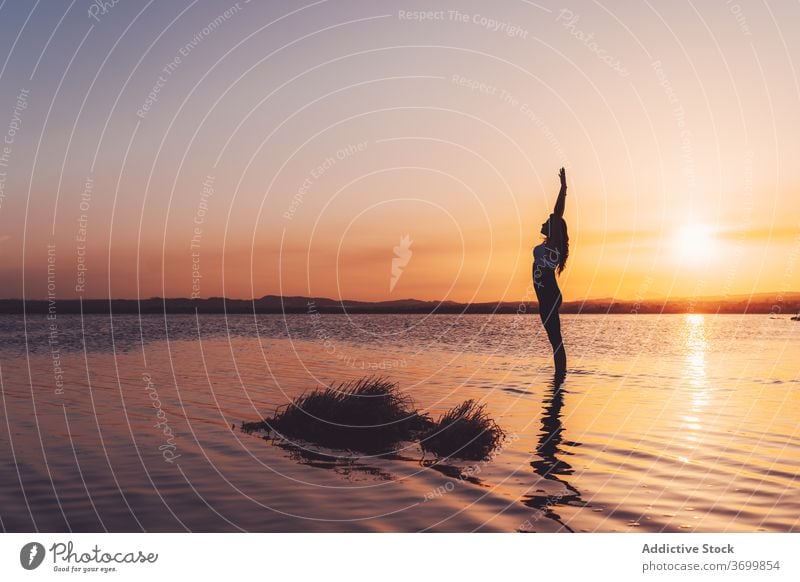 Focused woman with arms raised practicing yoga in lake water practice asana pose stand upward salute focus harmony Urdhva Hastasana balance calm wellness serene