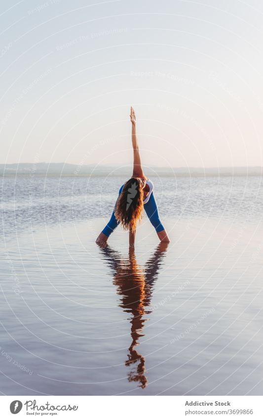 Woman performing yoga asana in lake water woman practice pose stand prasarita padottanasana forward bend revolved twist reflection focus harmony balance calm