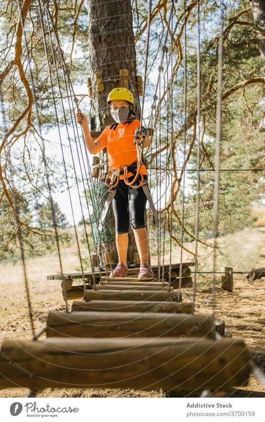 Child having fun in adventure park bridge suspension child safety equipment harness mask coronavirus rope kid carabine protect covid epidemic concentrate focus