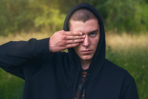 Portrait of a young man with a black hoodie covering his eyes portrait serious hand finger look teenager looking male beautiful casual caucasian outdoor