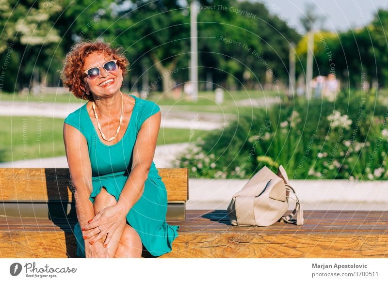 Mature woman sitting on the bench in the park in summertime 60s adult age aged alone beautiful beauty casual caucasian cheerful city confidence confident dress