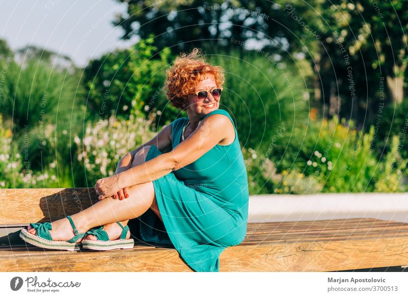 Mature woman sitting on the bench in the park in summertime 60s adult age aged alone beautiful beauty casual caucasian cheerful city confidence confident dress