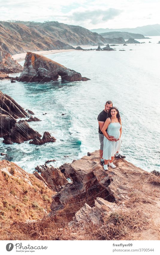 Pregnant couple on the edge of a cliff pregnant heterosexual romantic father mother parents woman contemplating hiking copy space landscape seascape loiba