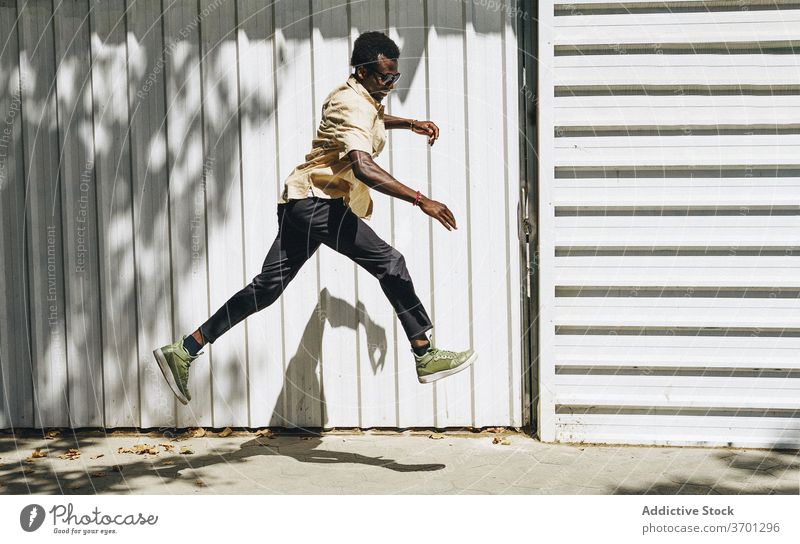 Cheerful ethnic man jumping on street carefree cheerful freedom sunny stroll city style male black african american barcelona spain building trendy town daytime