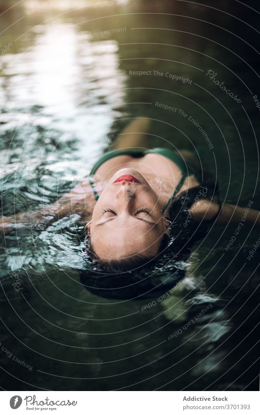 Serene woman floating on lake water swim enjoy vacation serene relax pond bikini female summer lying eyes closed swimwear rest recreation slim nature lady