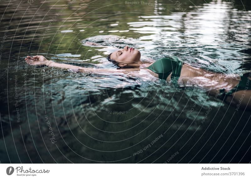 Serene woman floating on lake water swim enjoy vacation serene relax pond bikini female summer lying eyes closed swimwear rest recreation slim nature lady