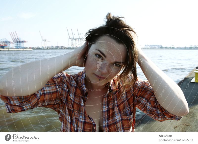 Young woman with freckles sitting on a pontoon in front of Hamburg harbour portrait Central perspective Looking brunette hair Copy Space right freckly Joy Model