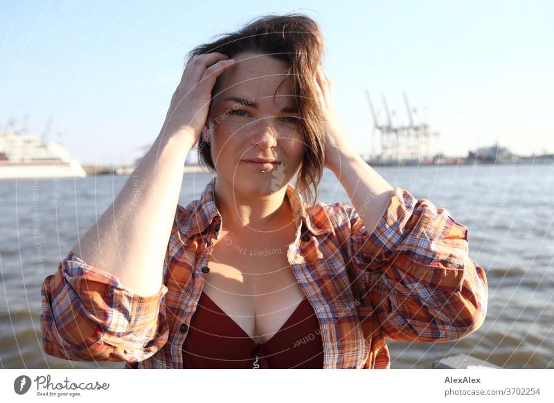 Young woman with freckles sitting on a pontoon in front of Hamburg harbour portrait Central perspective Looking brunette hair Copy Space right freckly Joy Model