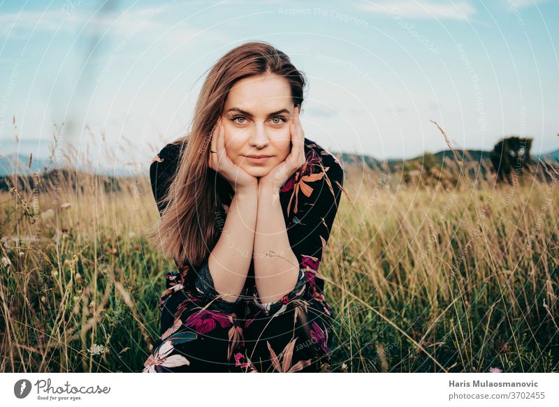 Blonde woman in flower dress looking ate the camera, sitting in the grass field adult beautiful beauty blonde blu sky caucasian face fashion female freedom girl