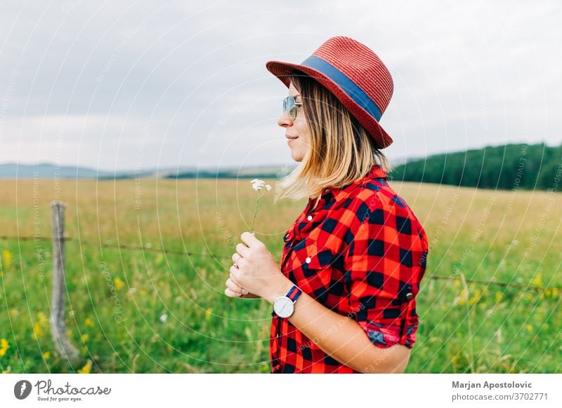 Young woman standing in a meadow with flower in her hands adult beautiful beauty blonde casual caucasian country countryside cute enjoying environment female