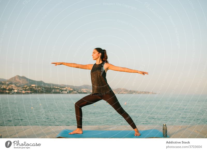 Calm woman in Warrior pose on yoga mat warrior pose virabhadrasana calm practice sea barefoot sportswear female tranquil amazing seascape wellness slim idyllic