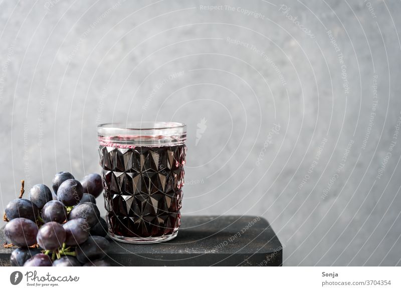 Fresh grape juice in a glass and blue grapes on a grey background Grape juice Glass Bunch of grapes Blue Beverage fruit Alcoholic drinks Vine Red wine Food