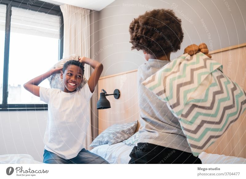 Two brothers playing with pillows at home. kids together happy bedroom excited portrait positive active pillow fight adorable lifestyle black happiness