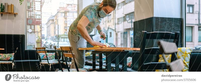 Waiter disinfecting tables due to coronavirus waiter cleaning covid-19 cafeteria restaurant worker banner web header panorama panoramic bar business man