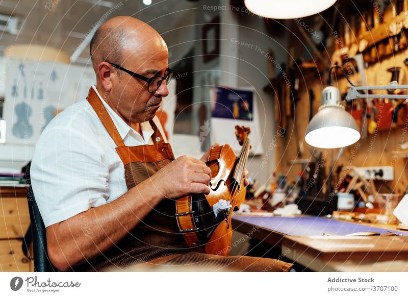 Craftsman with violin in professional workshop craftsman repair luthier artisan restore master skill male mature middle age maker handmade occupation workplace