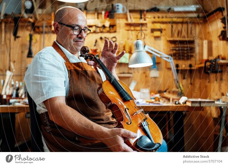 Craftsman with violin in professional workshop craftsman repair luthier artisan restore master skill male mature middle age maker handmade occupation workplace