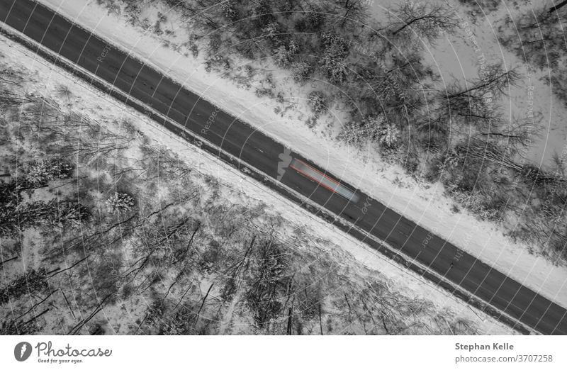 Aerial view on a winter street framed by snow, a car is passing by as a long exposure shot. road diagonal line lights schwaebische alb albstadt living drone