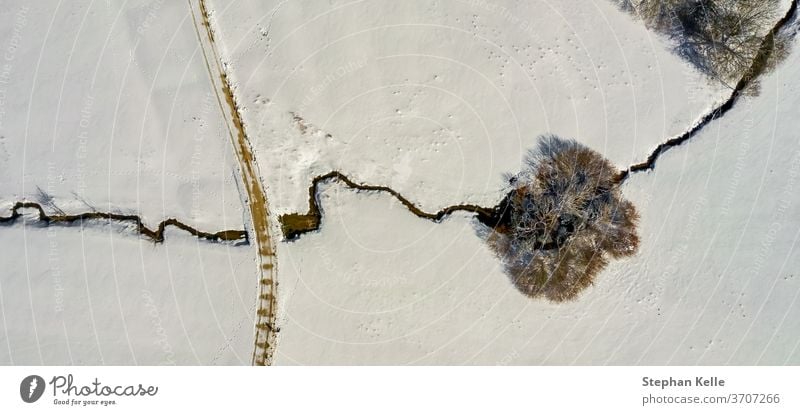 Winter scenery: A lonely tree crossed by a little creek , landscape full of snow. river winter single road alone copy space drone calm no person background