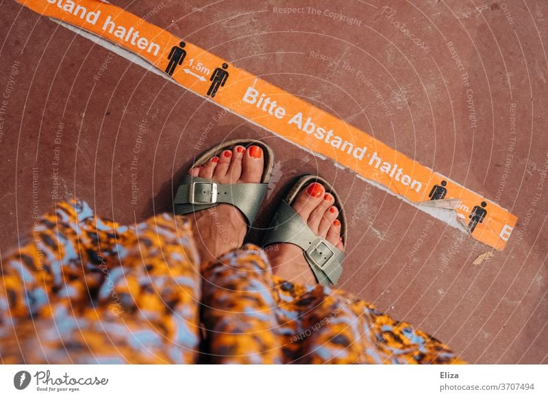 A woman stands in front of a distance marker in summer to keep her distance in times of Corona gap distance marking keep sb./sth. apart Retail sector Gastronomy