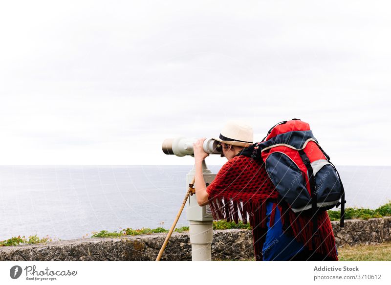 Backpacker admiring seascape through telescope woman pilgrimage hike backpack binocular travel observe explore camino de santiago spain activity seaside female