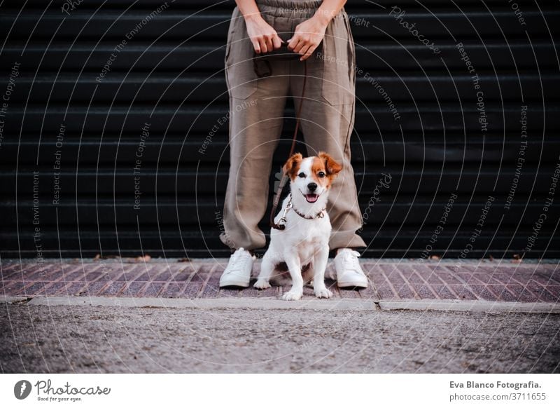 young woman outdoors wearing protective mask, cute jack russell dog besides. New normal concept street new normal pet walking urban city lifestyle corona virus