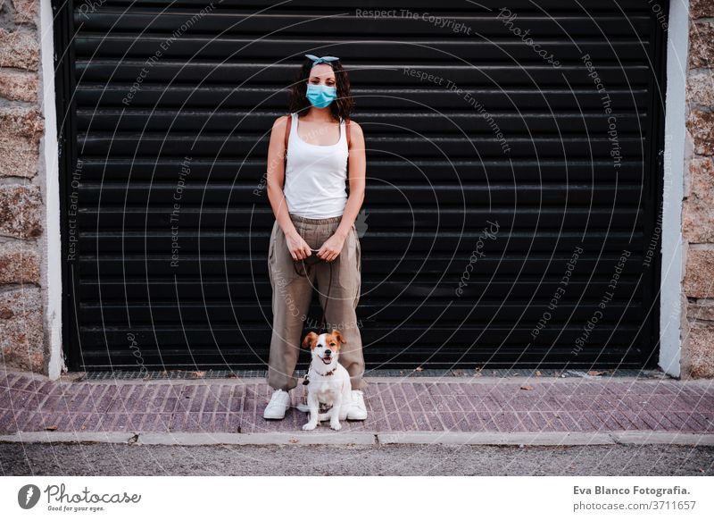 young woman outdoors wearing protective mask, cute jack russell dog besides. New normal concept street new normal pet walking urban city lifestyle corona virus