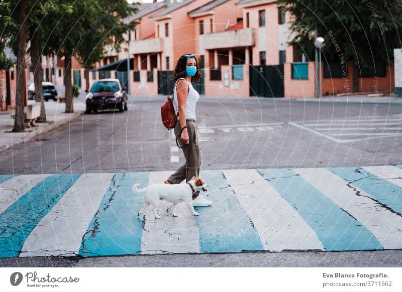 young woman walking by pedestrian crossing wearing protective mask, cute jack russell dog besides. New normal concept street new normal pet urban city lifestyle