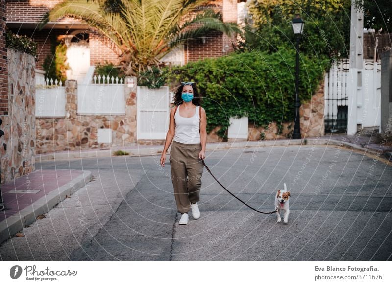 young woman walking outdoors wearing protective mask, cute jack russell dog besides. New normal concept street new normal pet urban city lifestyle corona virus