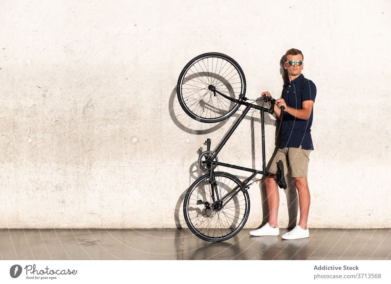 Man carrying his bicycle on concrete wall adult bike blond casual caucasian cycling cyclist lifestyle lean male man hold millennial mobility modern people