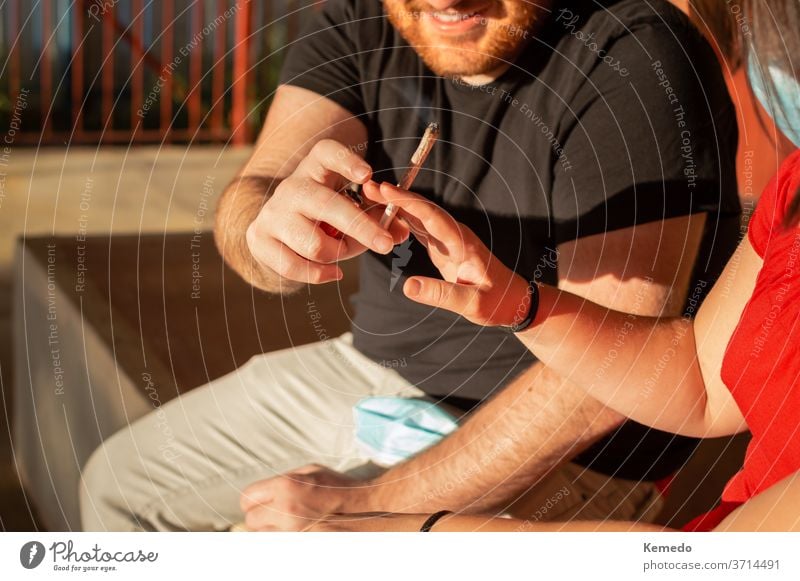 Young couple sharing a marijuana joint on the street during a sunset. pot cannabis smoke happy smile friends man boy guys outdoor hands give leisure beard