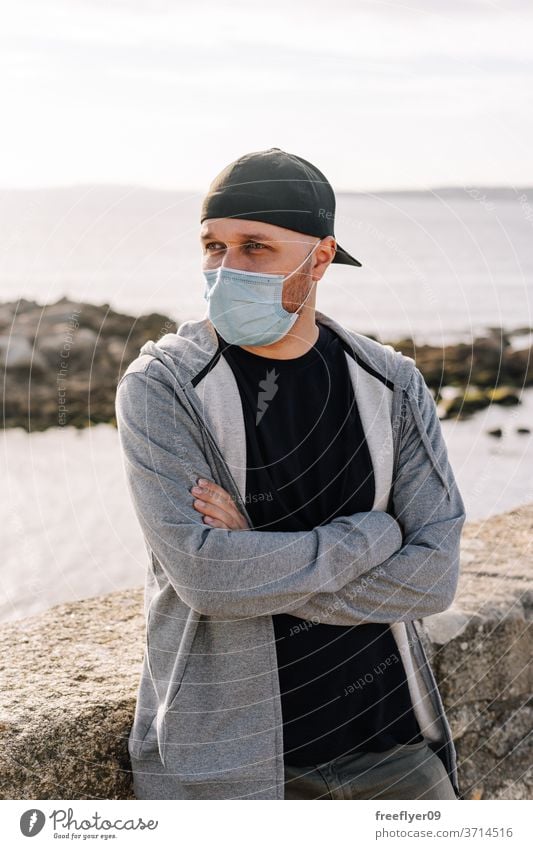 Tourist with a surgical mask near the ocean portrait man coast beach travel tourism tourist traveler pandemic coronavirus covid19 covid-19 sightseeing hat