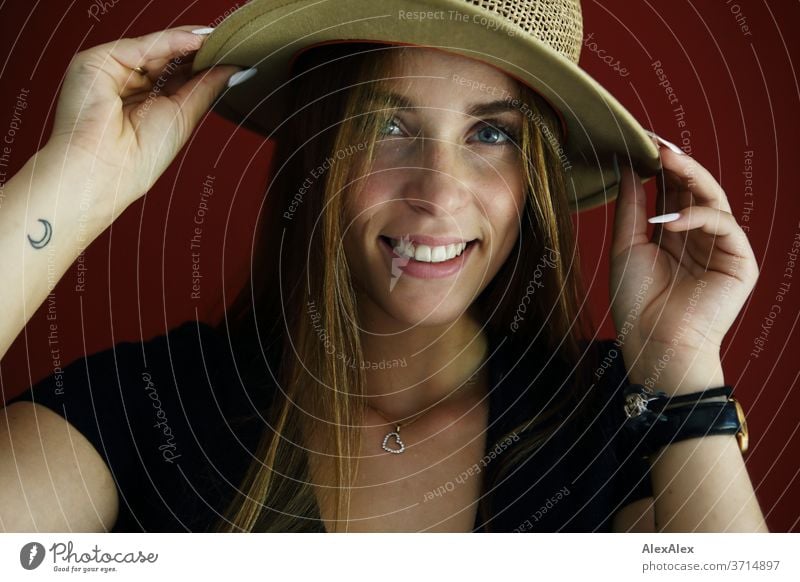 Direct portrait of a young woman in front of a red wall with a straw hat Athletic Feminine empathy Emotions emotionally Central perspective