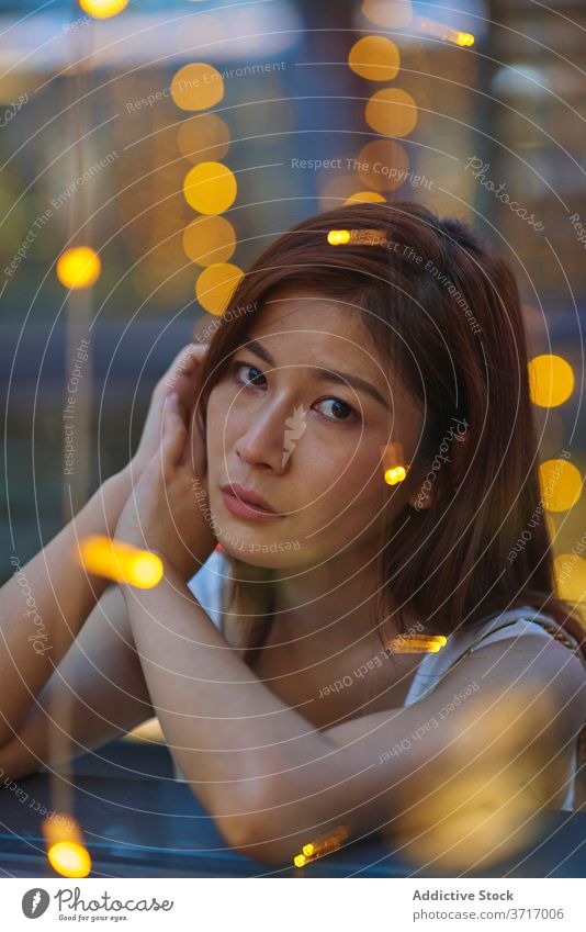 Thoughtful woman in cafe in evening thoughtful pensive city garland calm weekend window female asian ethnic lean relax rest tranquil peaceful style cozy trendy