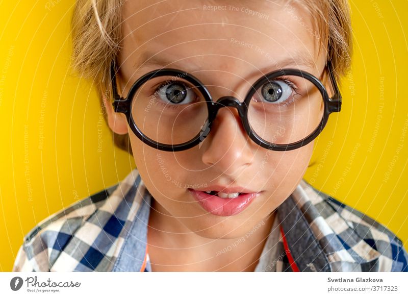 Portrait of cute and clever blonde Caucasian boy in a checked shirt on yellow background. 1 September day. Education and back to school concept. Child pupil ready to learn and study.