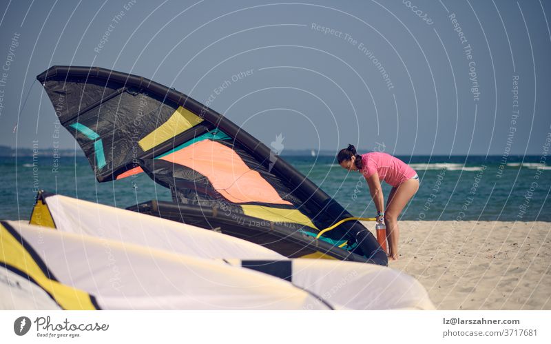 Middle-aged woman pumping up up a kitesurfing kite at the beach on summer vacation in hot sunshine with ocean backdrop middel-aged warm inflating kiteboarding