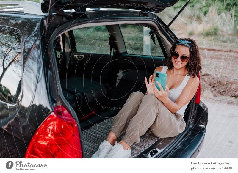 young happy woman in a car using mobile phone. Travel concept travel caucasian smiling outdoors waiting adult contraption communication lifestyle sitting