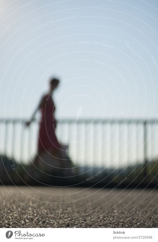 Young woman walks with bag in front of a railing over asphalt strong blur Woman Going Profile blurred Asphalt Sky Blue Dress Summer Back-light Silhouette