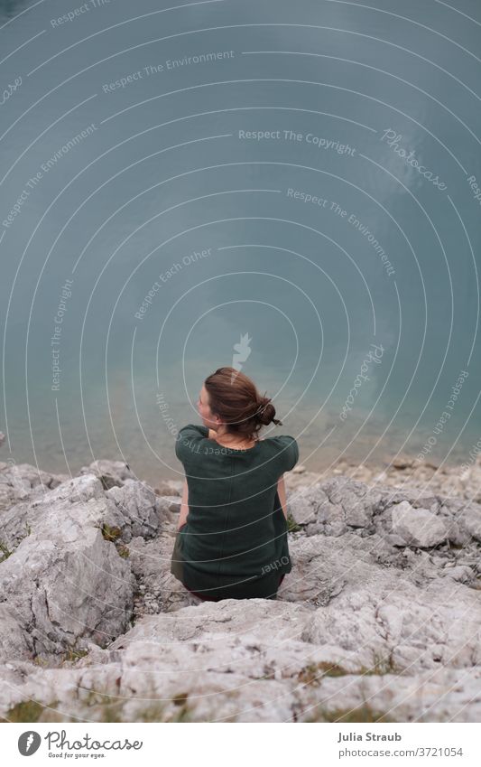 Woman sitting on light rocks on the shore of the Alpsee Bird's-eye view Above Lünersee petrol green turquoise grey-blue Brown Gray Stony Rock sedentary look