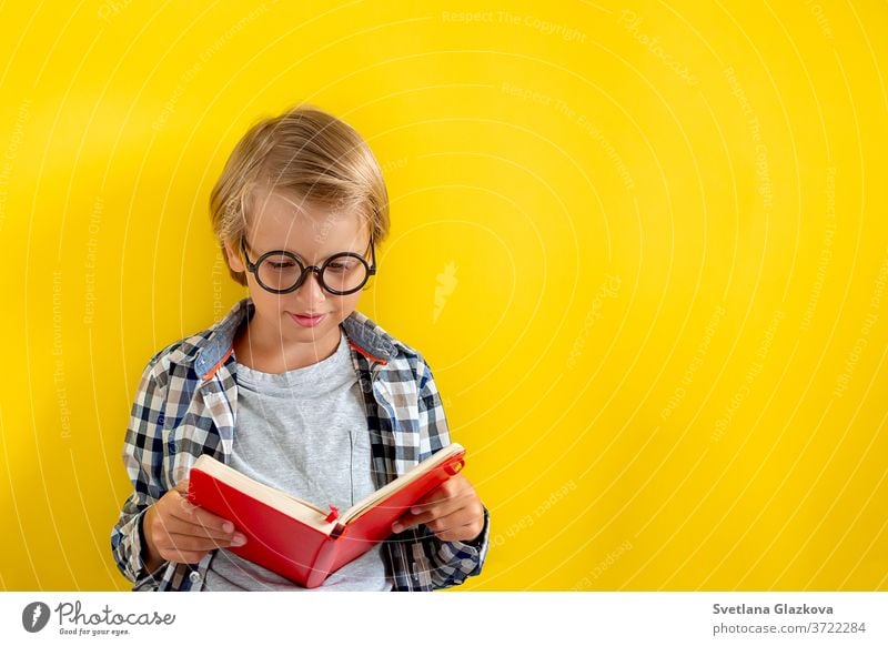 Portrait of cute and clever blonde Caucasian boy in a checked shirt on yellow background. 1 September day. Education and back to school concept. Child pupil ready to learn and study.