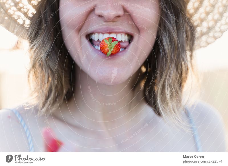 closeup of the mouth of a young farmer woman biting a freshly picked ripe strawberry from its plant in an organic vegetable garden healthy lifestyle close-up