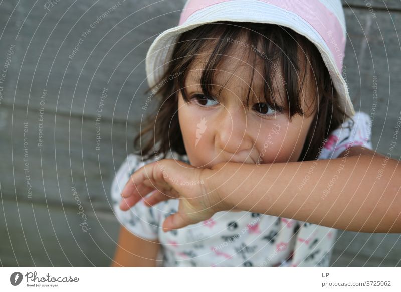 girl wearing a hat holding her hand on her mouth Girl Looking Upper body Portrait photograph Neutral Background Close-up Exterior shot Subdued colour