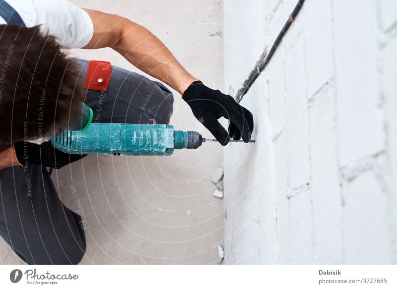 Man worker drilling wall with hammer drill, top view renovation repairs man male adult power tool holding home hole handyman indoor builder white house interior