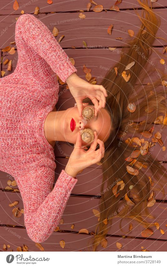 Where is fall ? Young woman lying on a wooden deck, covering her eyes with huge acorns. having fun model natural fashion face portrait leaf autumnal holiday